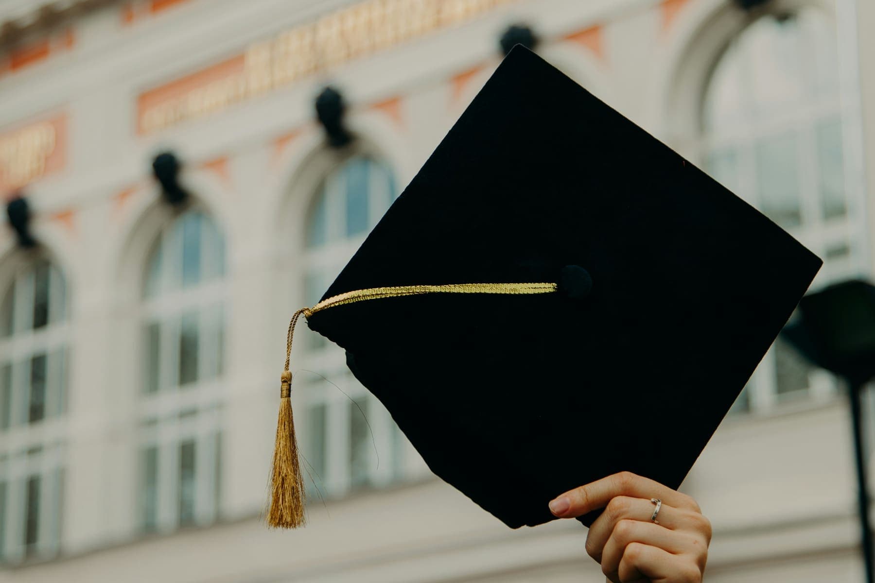 A graduation cap held up in the air outside a university building